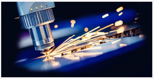 A close-up of a laser cutting machine emitting sparks as it cuts through a sheet of metal, illustrating a high-precision industrial manufacturing process.